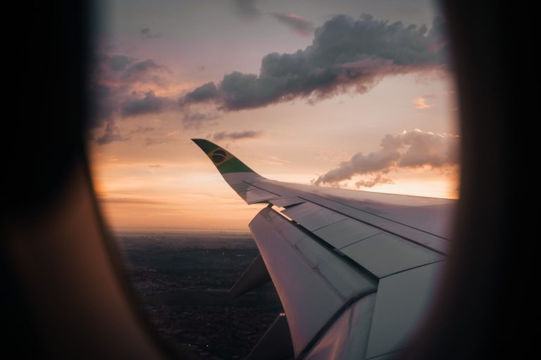 Baixa temporada reduz em 31% o preço médio de voos domésticos Vista da asa de um avião pela janela, contra o céu ao entardecer.