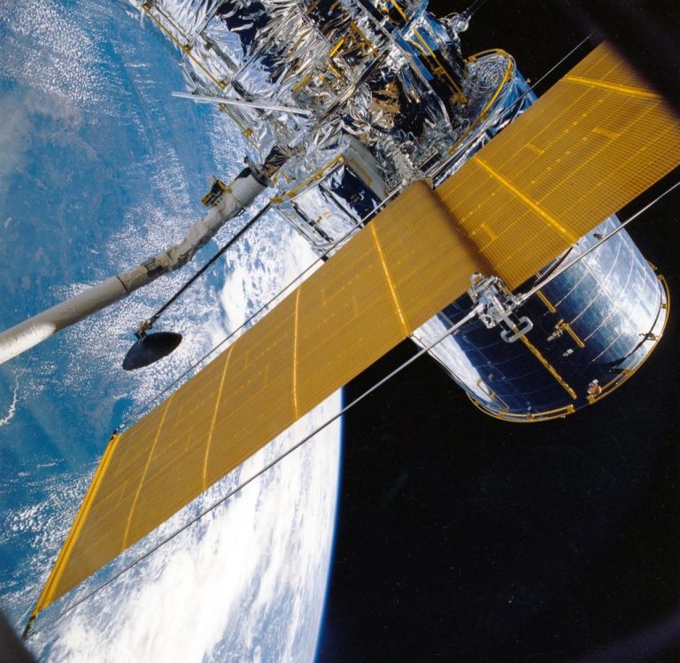 Espaçonave com painéis solares orbitando a Terra contra o fundo escuro do espaço.